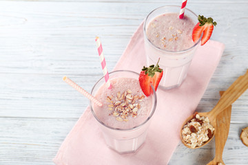 Wall Mural - Glasses of tasty strawberry milkshake on napkin and white wooden background