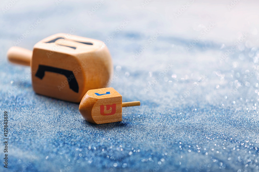 Wooden dreidels for Hanukkah on light sparkling background