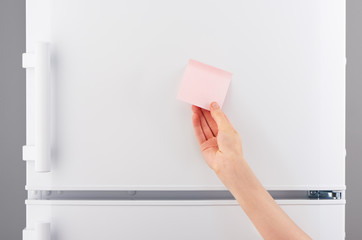 female hand holding pink paper note on white refrigerator