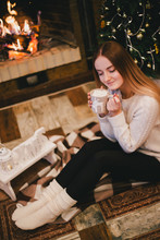 Beautiful Young Woman Sitting Near Fireplace Under The Christmas Tree Drinking Cocoa With Marshmallow. Cozy Mood