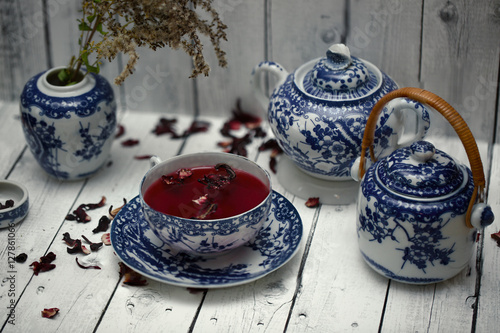 Fotografie, Obraz Set of decorative porcelain dishes, cups, plates, teapot with blue ethnic pattern in the style of Chinese painting with red karkade tea