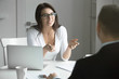 © fizkes - Young friendly smiling businesswoman wearing glasses talking to a male candidate at the desk, interviewing a job applicant. Rear view at a man. Business concept photo