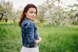 Young pretty sexy caucasian woman in white dress and denim jacket walks in a blooming spring garden on sunset. Youth, freshness, beauty, romance, happiness concept.