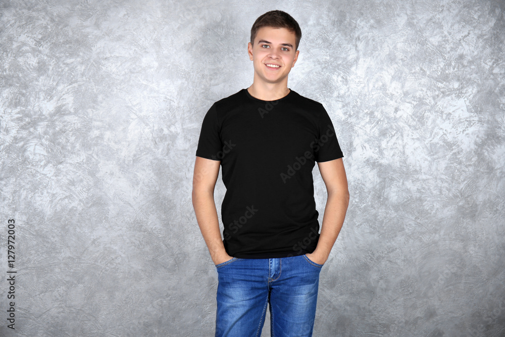 Handsome young man in blank black t-shirt standing against grey textured wall
