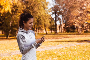 Happy girl texting on a smart phone in the park while waiting fo