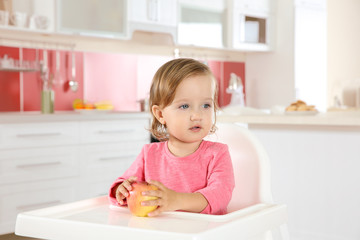 Poster - Cute little girl with apple in high chair at kitchen