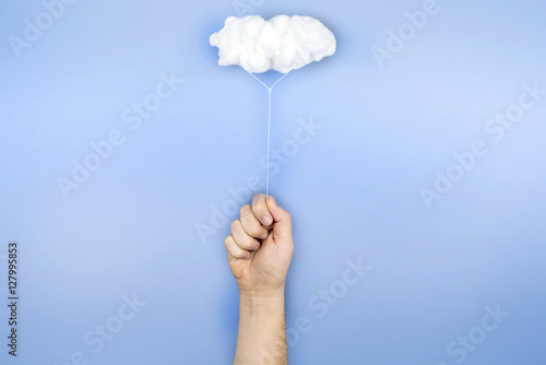 Fotografie, Obraz Mano sujetando una nube que hace de globo sobre fondo azul.