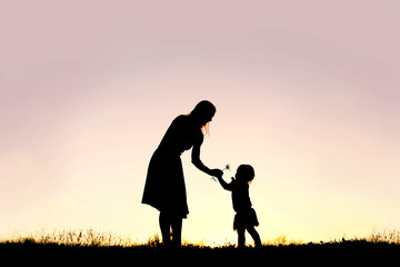 silhouette of baby girl giving mom flower at sunset