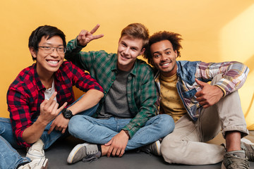 Wall Mural - Three smiling men friends showing thumbs up and peace gestures