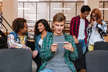 Sticker - Attractive young man using smartphone while students standing and talking