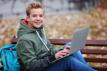 Poster - Teenager with laptop sitting on bench in autumn park