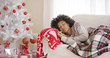 © Dash - Single Black woman in sweater and plaid blanket sleeping on couch beside white Christmas tree