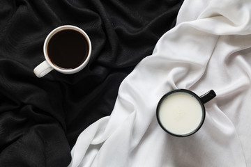 Two cups of coffee and milk on the black or white fabric. Top view.