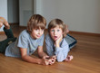 © Tatiana Murr - Two surprised kids lying on wooden floor and using mobile phone