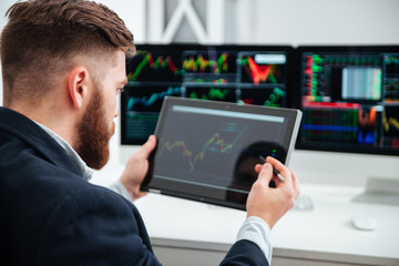 Back view of bearded businessman woking with tablet in office