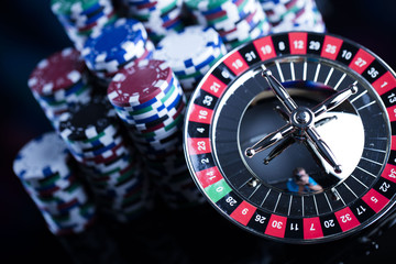 Casino theme. High contrast image of casino roulette, poker game, dice game, poker chips on a gaming table, all on colorful bokeh background. Place for typography and logo.