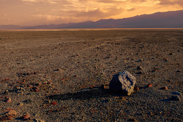 Wall Mural - A lone boulder lies in an expansive, empty desert at sunset