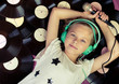 Beautiful girl lying next to vinyl records holding a microphone and listening music on headphones.