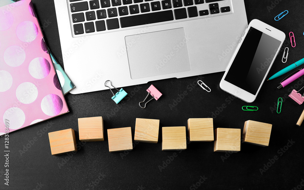 Laptop, copybook and wooden cubes on color background