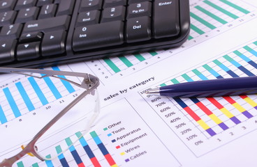 Pen, glasses and computer keyboard on financial graph, business concept