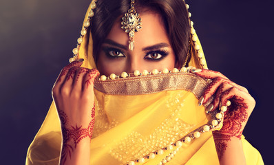 Wall Mural - Beautiful indian girl . Young hindu woman model  with tatoo mehndi  and kundan jewelry . Traditional Indian costume yellow saree . Indian or Muslim woman covers her face.