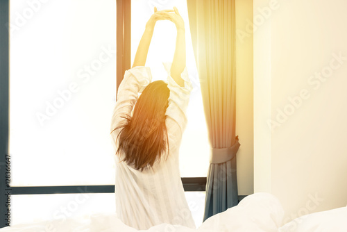 Fotografie, Obraz Rear view of woman stretching in bed after wake up in morning with sunlight