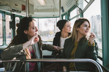 Three beautiful young women sitting in tram and looking through window.