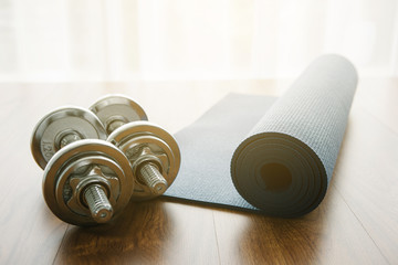 Silhouette Pair of dumbbells with blue yoga mat on wood floor,flare light