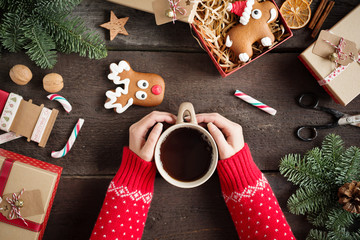 Wall Mural - Woman holding in hands hot christmas tea with candy cane against decorations, gift boxes, ribbon and ginger bread on wooden board. Xmas concept. Eye bird view. 