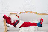 Fototapeta  - Santa Claus resting on a sofa at home.