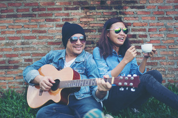 Hipster man playing guitar for his girlfriend outdoor against br