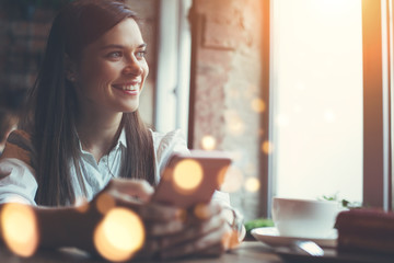 Smiling woman in cafe using mobile phone and texting in social networks, sitting alone