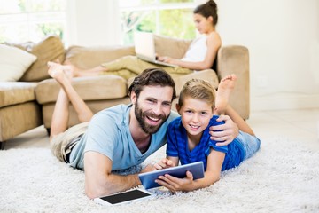 Portrait of father and son lying on rug and using digital tablet