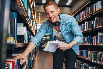 Wall Mural - Young man at bookshelf at public library