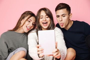 Wall Mural - Young beautiful friends making selfie on tablet over pink background.