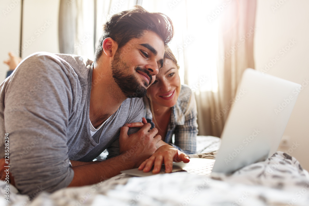 Young married couple lying on bed at home and using laptop. Stock Photo ...
