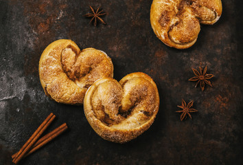 Wall Mural - Cinnamon rolls in the form of heart on a dark metallic rusty background with cinnamon sticks and anise stars. Selective focus. Toned image 