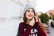 © Look! - Closeup portrait pretty brunette with long hair in knitted hat and marsala sweater speaking on phone on street. She is smiling to side