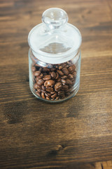 Sticker - Transparent glass coffee jar filled with beans of coffee over the dark wooden table.