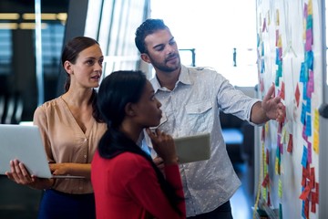 Team of colleagues standing by white board reading sticky notes