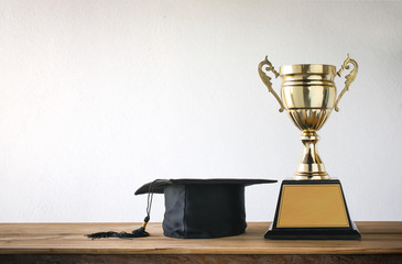 graduation cap with champion golden trophy on wood table with co