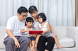 © Tan Kian Khoon - Asian Chinese parents and daughters reading book on the sofa