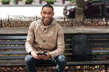 Wall Mural - Happy man holding tablet while sitting on wooden bench