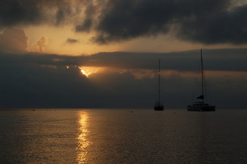 View of the sunset in a cloudy sky on the sea with the silhouette of two boats, Italy