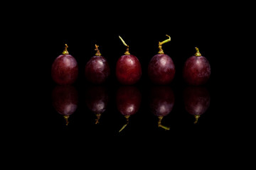 Five red grapes isolated on black background