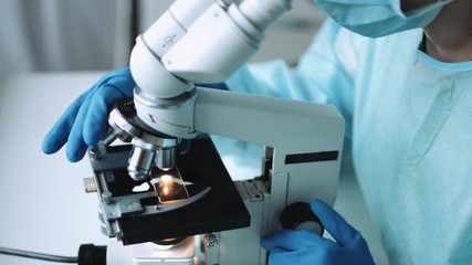 Wall Mural - scientist in blue medical gloves and uniform learning samples with microscope in laboratory.