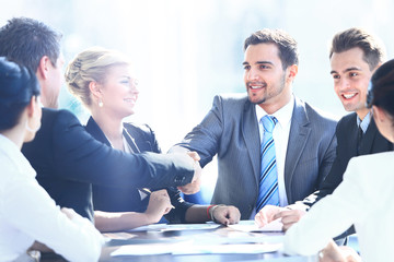 Wall Mural - Business colleagues sitting at a table during a meeting with two male executives shaking hands