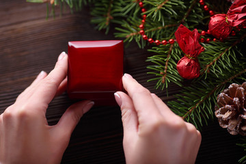 Engagement ring in female hands among Christmas decorations on wood background