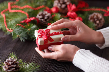 Beautiful female hands holding a Christmas present in box with red bow.