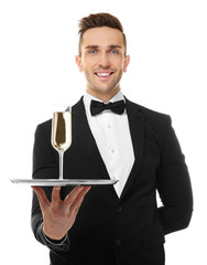 Canvas Print - Handsome young waiter holding tray with glass of champagne, on white background